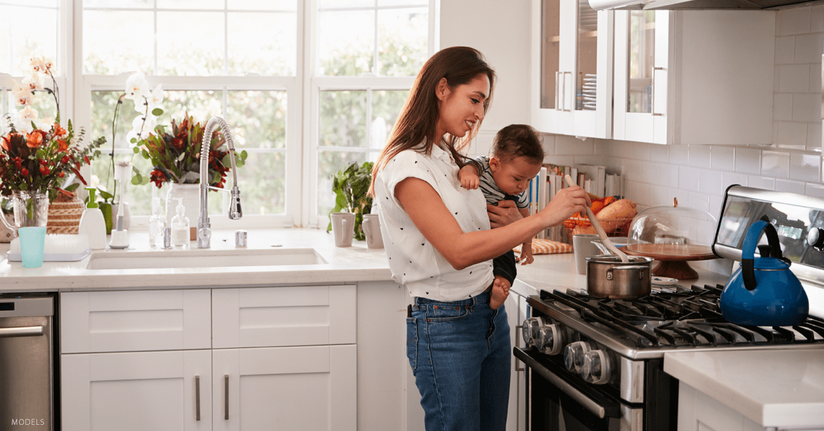 Mom holding her baby while cooking and considering a mommy makeover