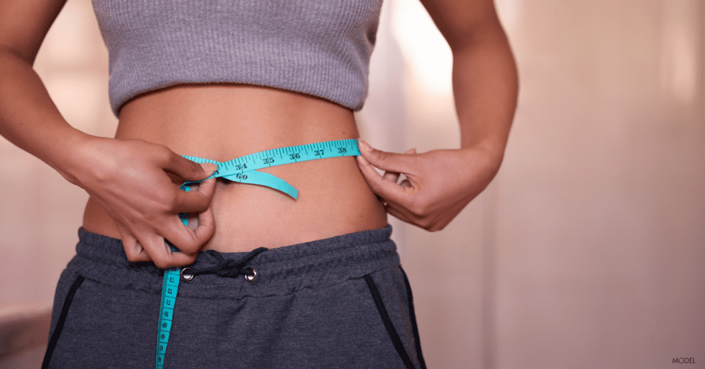 Young woman measures waist and examines weight after liposuction procedure.