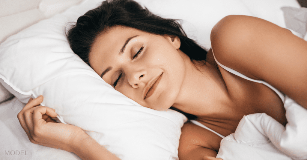 Beautiful young woman smiling during sleeping while lying in the bed at home (model)
