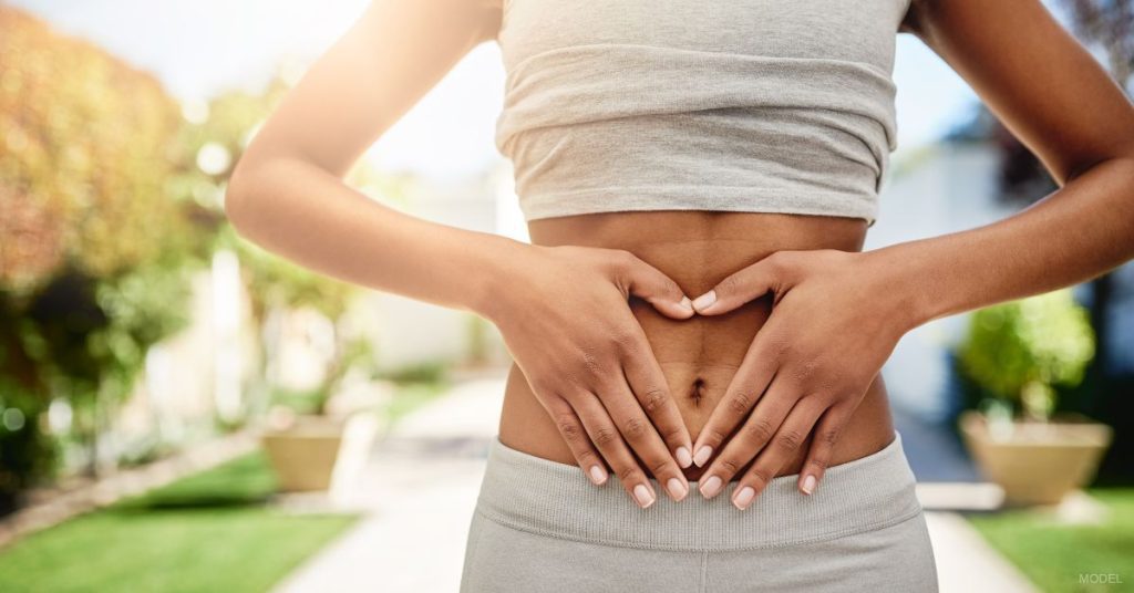 A woman with their hands on their stomach. (Model)